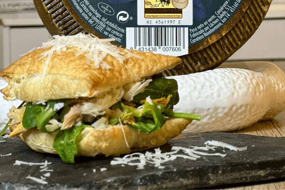 un miguelito con queso manchego en una tabla negra con un queso manchego detrás.